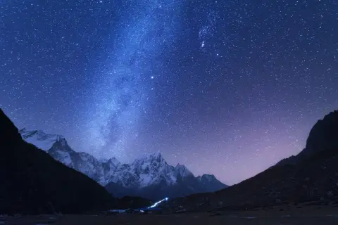 Magnifique photo de nuit. Le ciel étoilé scintille au-dessus de montagnes enneigées et d'un petit village illuminé.
