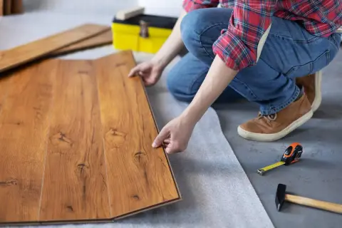 Man instalando suelo de tarima flotante. Se ven las lamas de madera, una cinta métrica y un martillo.