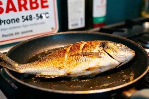 Poisson entier doré dans une poêle, prêt pour une recette gastronomique facile.