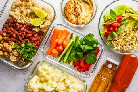 Gotowe jedzenie pod namiot: ryż z fasolą i pieczarkami, warzywa pokrojone w słupki, kalafior, sałatka z pomidorami i awokado, hummus, soki.