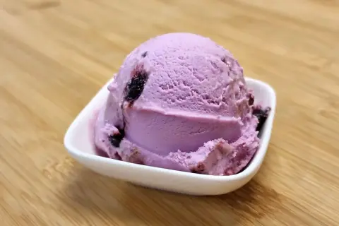 Ein Löffel Amarena-Eis mit Fruchtstückchen, das leicht nach Alkohol duftet, in einer weißen Schale auf Holzuntergrund.
