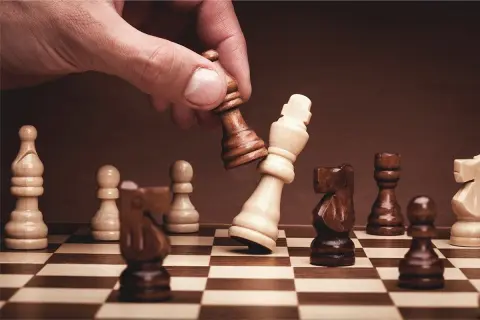 Dłoń gracza wykonuje ruch, przewracając białego króla. To kluczowy moment, ilustrujący zasady gry w szachy i strategię.