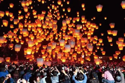 Tysiące lampionów unosi się na nocnym niebie, tworząc magiczny widok podczas święta lampionów. Tłum ludzi obserwuje to widowisko.