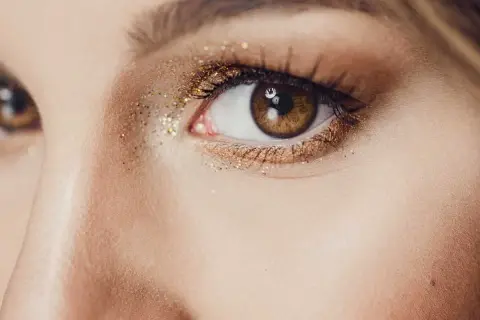 Un œil marron orné d'un maquillage soirée doré scintillant, parfait pour briller toute la nuit.