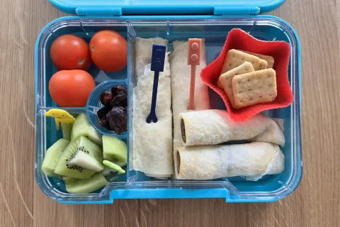 Kolorowe śniadaniówkowe pudełko dla dzieci: pomidorki, kiwi, suszone śliwki, naleśniki z czekoladą i ciasteczka. Idealne na drugie śniadanie!