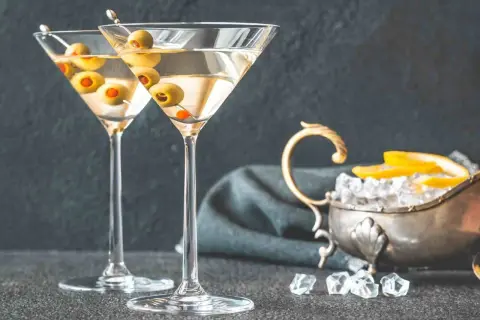 Dwa kieliszki z martini, ozdobione oliwkami, czekają na degustację. Obok lód i cytryna, idealne dodatki, by dowiedzieć się, jak pić martini.