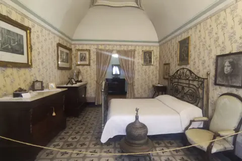 Camera da letto nella casa di d'Annunzio, con carta da parati floreale, letto in ferro battuto e mobili d'epoca.