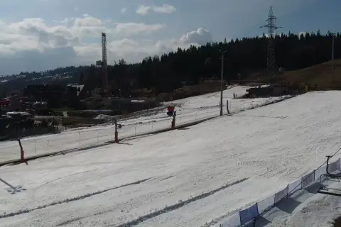Widok z białka tatrzańska webcam na ośnieżony stok narciarski z wyciągiem krzesełkowym i wieżą w tle.