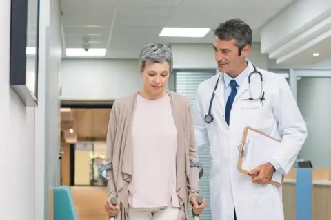 Lekarz wspiera pacjentkę po urazie, która porusza się o kulach. Postęp w leczeniu traumatologii jest widoczny.