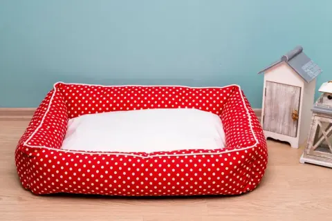 Rotes Hundebett mit weißen Punkten und weißer Liegefläche, bereit fürs hundebett waschen. Daneben stehen Deko-Häuschen.