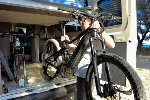 Hombre cargando una bici eléctrica en una furgoneta. Así es como llevar la bici dentro de la furgoneta para tus aventuras.