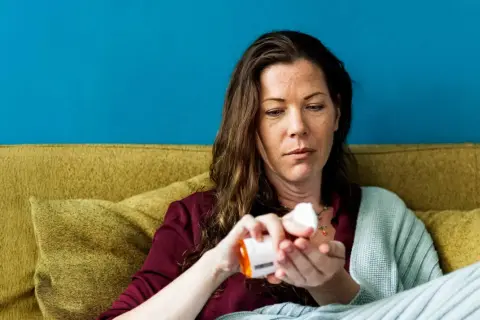 Vrouw neemt medicatie, hopend dat werkt bachbloesem echt. Ze zit op een bank met een deken.