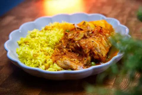 Herzhaftes Sudado de Pollo mit gelbem Reis und Erbsen, serviert in einer weißen Schale auf einem Holztisch.