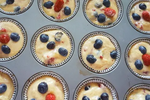 Frisch zubereiteter Teig für Heidelbeer Muffins, mit saftigen Blaubeeren und roten Beeren in einer Muffinform.