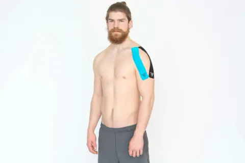 Homme avec un taping bleu et noir sur l'épaule, pour le soutien de la coiffe rotateur.