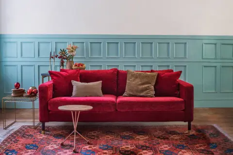 Ein rotes Samtsofa mit braunen Kissen vor einer blau getäfelten Wand. Welche Farbe passt zu Rot? Braun und Blau sind eine tolle Wahl!