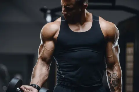 Ein Mann mit beeindruckenden **Armmuskeln** hebt eine Hantel im Fitnessstudio. Seine Bizeps und Unterarme sind stark definiert.