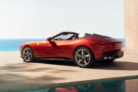 Czerwony Ferrari Spider z otwartym dachem, zaparkowany przy basenie z widokiem na morze.