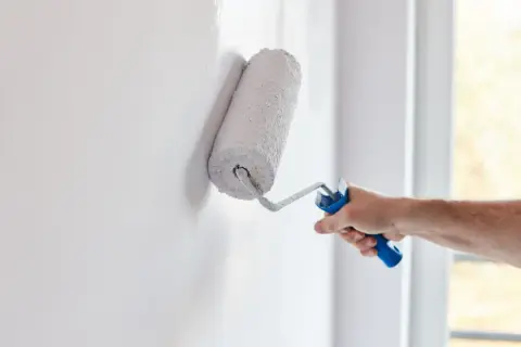 Mano aplica pintura aterciopelada blanca a una pared con un rodillo.