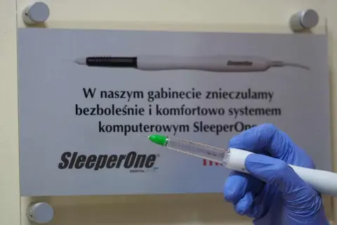 Ręka w niebieskiej rękawiczce trzymająca komputerowy system znieczulający SleeperOne.