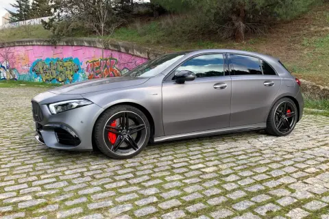 A45 AMG CV gris mate, con pinzas rojas y llantas negras, aparcado sobre adoquines frente a un muro con grafitis.