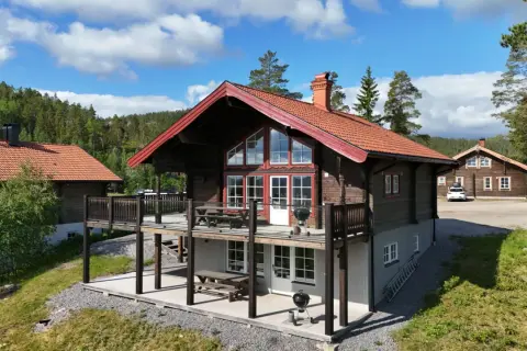 Träfasade hus med röda tak och stora fönster, belägna i en skogsmiljö. En härlig plats att bo på, kanske vid alpstigen i Järvsö.