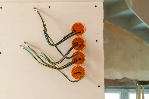 Instalacja elektryczna w domku drewnianym w trakcie prac. Widoczne puszki instalacyjne i przewody.