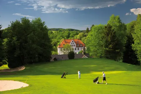 Zwei Golfer auf dem grünen Rasen des Golfclubs Schloss Georghausen, im Hintergrund das malerische Schloss.