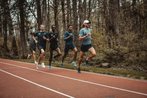 Cinq coureurs s'entraînent sur une piste, leurs foulées rythmées par un entraînement de fractionné course intense.