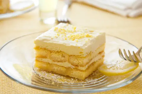Ein Stück Limoncello Tiramisu auf einem Teller, garniert mit Zitronenschale. Ein Hauch von Sommer auf jedem Löffel.