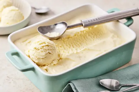 Ein Behälter mit cremigem Vanilleeis, perfekt zum vanilleeis selber machen. Ein Löffel liegt bereit, um die erste Kugel zu entnehmen.