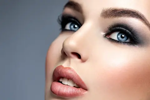Niebieskie oczy podkreślone intensywnym, ciemnym smokey eye i długimi rzęsami. Usta w odcieniu nude.