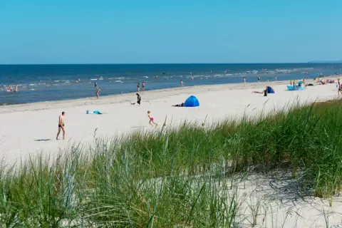 Menschen genießen einen sonnigen Tag am Strand der Ostsee. Nach der Fahrt mit dem Zug von Berlin ist dies eine willkommene Erfrischung.