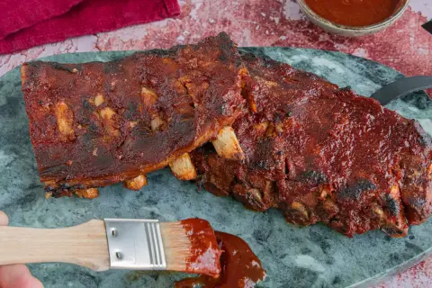 Saftige Spareribs sous vide, glasiert mit BBQ-Sauce. Ein Pinsel mit Sauce liegt daneben.