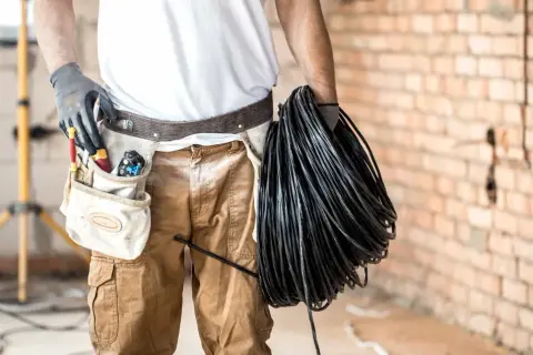 Elektryk z pasem narzędziowym trzyma zwój czarnego kabla. Czy kabel ziemny musi być w peszlu? To pytanie, na które odpowiedź zależy od wielu czynników.