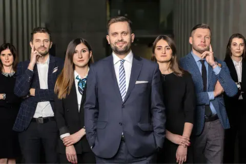 Grupa prawników w eleganckich strojach stoi przed nowoczesnym budynkiem.