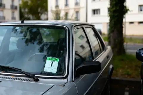 Autocollant de contrôle technique périmé 1 mois sur le pare-brise d'une voiture grise.