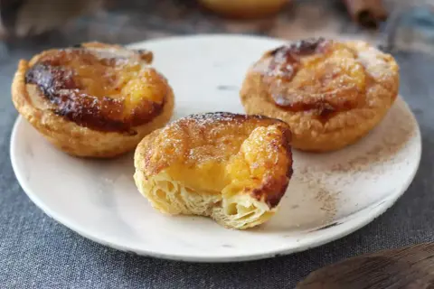 Tre gyllene pastel de nata med krämig fyllning och karamelliserad yta, pudrade med florsocker.