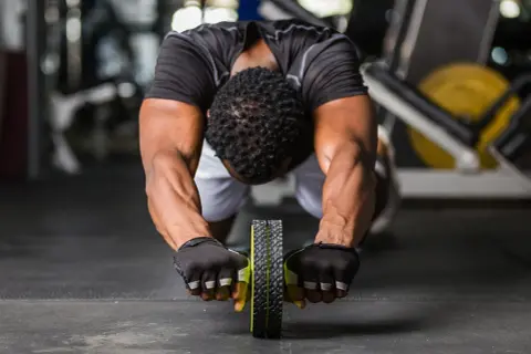 Man gör en ab wheel rollout i gymmet, med fokus på magmusklerna.