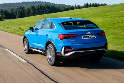 Niebieskie Audi Q3 Sportback jedzie po krętej drodze wśród zielonych wzgórz. Poznaj jego wymiary.