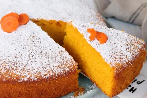 Una fetta di torta Camilla, soffice e arancione, cosparsa di zucchero a velo e decorata con carote.