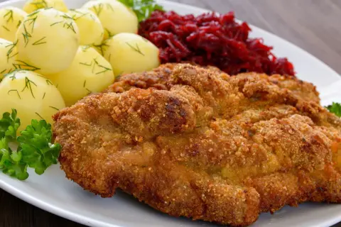 Kotlet schabowy w panierce z ziemniakami i buraczkami na białym talerzu.