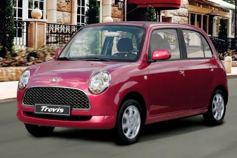 Czerwony Daihatsu Trevis z charakterystyczną kratką i okrągłymi światłami pędzi ulicą przed eleganckim budynkiem.