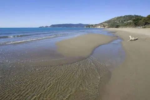 Le **spiagge** dorate dell'**Argentario** incontrano il mare cristallino, con un ruscello che serpeggia sulla **sabbia**.