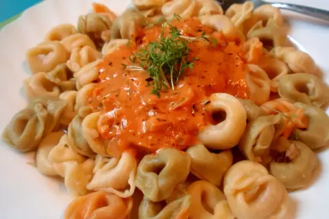 Kolorowe tortellini w kremowym sosie pomidorowym, udekorowane świeżą rukolą. Pyszny sos do tortellini kusi aromatem.
