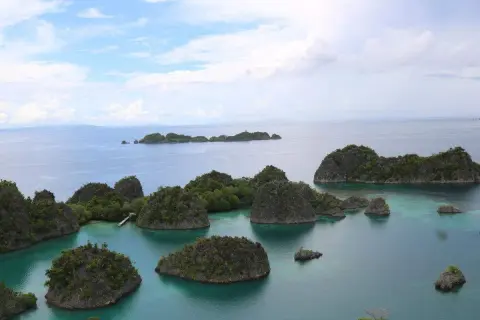 Grüne Inseln ragen aus türkisfarbenem Wasser, eine malerische Aussicht, die man vom Raja Ampat Flughafen aus genießen kann.