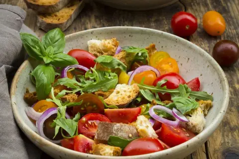 Bunter Salat mit Tomaten, Brotstücken und Rucola, verfeinert mit einem Hauch Balsamico Dressing.