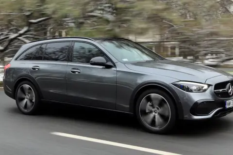 Szary Mercedes All-Terrain z napędem 4matic pędzi po drodze, zaśnieżone drzewa w tle.