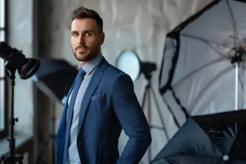 Elegancki mężczyzna w garniturze pozuje w studiu fotograficznym. W tle widać sprzęt oświetleniowy, idealny do stworzenia profesjonalnego packshotu i cennika.