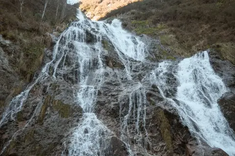 La cascada de Aitzondo desciende por una ladera rocosa, con agua blanca y espumosa que se abre paso entre la vegetación seca y las rocas grises.